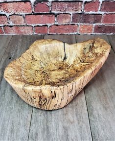 a wooden bowl sitting on top of a wooden table next to a brick wall and floor