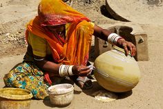 a woman sitting on the ground next to some pots and buckets with something in them