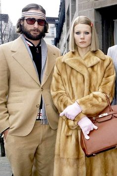 three people standing next to each other in front of a building wearing fur coats and hats