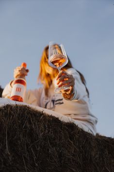 a woman sitting on top of a pile of hay holding a wine glass in her hand