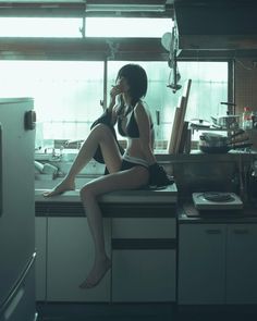 a woman sitting on top of a kitchen counter next to a stovetop oven and sink