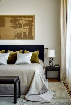 a bed with white and green pillows in a bedroom next to a painting on the wall