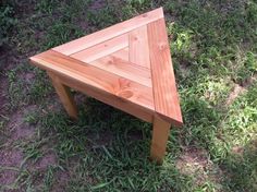 a wooden table sitting in the grass on top of a patch of green grass next to a field