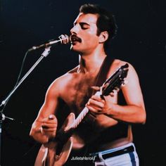 a shirtless man holding a guitar while singing into a microphone