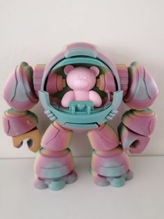 a pink and blue toy with a teddy bear in it's mouth on a white surface