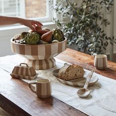 a table topped with plates and cups filled with food next to a person reaching for something