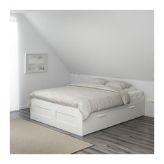 a white bed sitting in the middle of a bedroom under a slanted ceiling next to a window