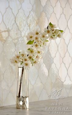 white flowers are in a clear vase on a table next to a wallpapered background