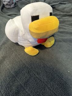 a stuffed ducky sitting on top of a bed next to a gray comforter