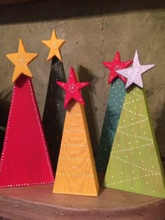 three small wooden christmas trees with stars on them, each decorated in different colors and sizes