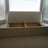 an empty bed frame in the corner of a room with two windows and shutters