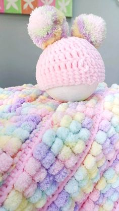 a crocheted blanket with two pom poms on it and a stuffed animal in the middle