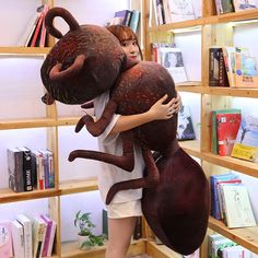 a woman holding two stuffed animals in front of a bookshelf filled with books