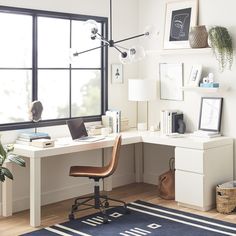 a desk with a laptop on it in front of a large window and a rug