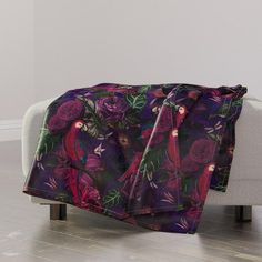 a purple and green blanket sitting on top of a white couch next to a wall