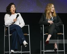 two women sitting in chairs with microphones on their laps and one is speaking to the other