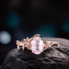 a pink stone ring sitting on top of a rock with leaves and vines around it