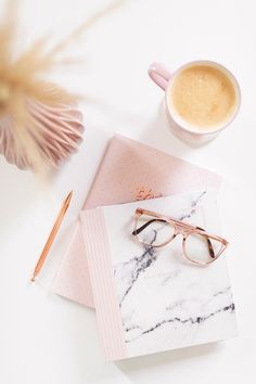 a cup of coffee next to a pair of glasses on top of a marbled notebook