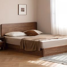 a bed sitting next to a window in a room with wooden floors and white walls