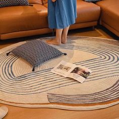 a woman standing in front of a couch looking at a magazine on top of a rug