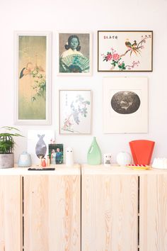 there are many framed pictures on the wall above this wooden cabinet, and vases