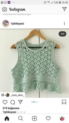 a green top with crocheted details on the front and bottom, hanging from a wooden hanger