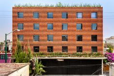 an orange brick building with lots of windows and plants growing on the top of it