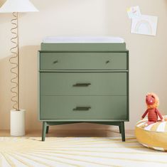 a baby's room with a green dresser and yellow pillow on the floor next to it