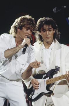 two men in white outfits are holding guitars and singing into microphones while standing next to each other