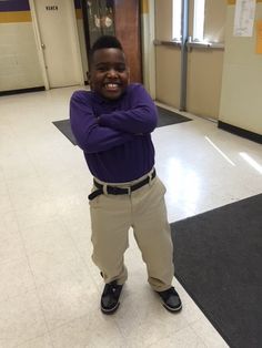 a young boy standing in a hallway with his arms crossed and smiling at the camera