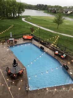 an outdoor swimming pool surrounded by lawn furniture and string lights at the end of it