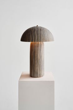 a striped lamp sitting on top of a white block in front of a gray wall