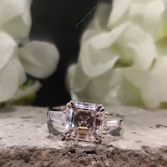 an engagement ring sitting on top of a rock with white flowers in the back ground