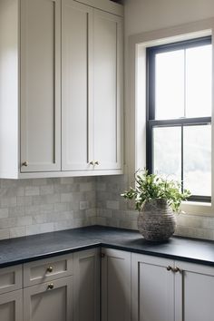 a kitchen with white cabinets and black counter tops is pictured in this image, there are a potted plant on the window sill