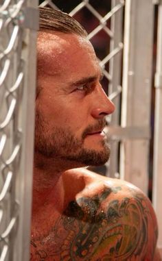 a close up of a man with tattoos on his arm and chest behind a chain link fence