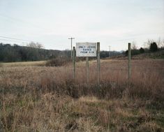 a sign in the middle of an empty field with no grass and trees around it