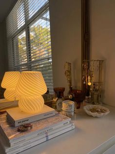 a lamp sitting on top of three books next to a window with blinds in the background