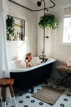 a child sitting in a bathtub next to a table and potted plants on the wall