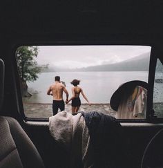 two people standing in the back seat of a car looking out at a body of water