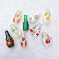 small glass bottles are lined up on the floor next to each other, with fruit and flowers painted on them