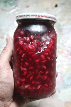 a hand holding a jar filled with pomegranate