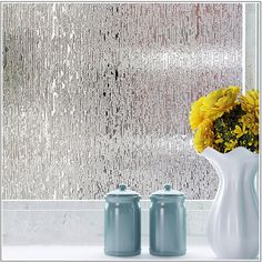 two white vases with yellow flowers in front of a rain - streaked glass wall