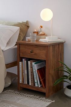 a night stand with books on it next to a bed and a plant in the corner