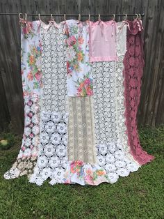 a quilt hanging on a clothes line in the grass next to a fence with flowers