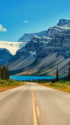 an empty road with mountains in the background and trees on both sides that are painted yellow