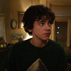 a young man with curly hair wearing a green t - shirt looking at the camera