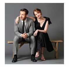 a man and woman are sitting on a bench posing for a photo in front of a gray background