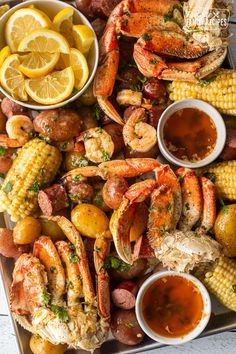 the seafood platter is ready to be served with corn, potatoes and lemon wedges