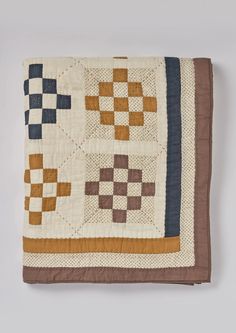 a brown and white quilt with squares on the front is laying on top of a table