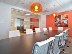 an empty conference room with orange walls and white chairs in front of a large wooden table